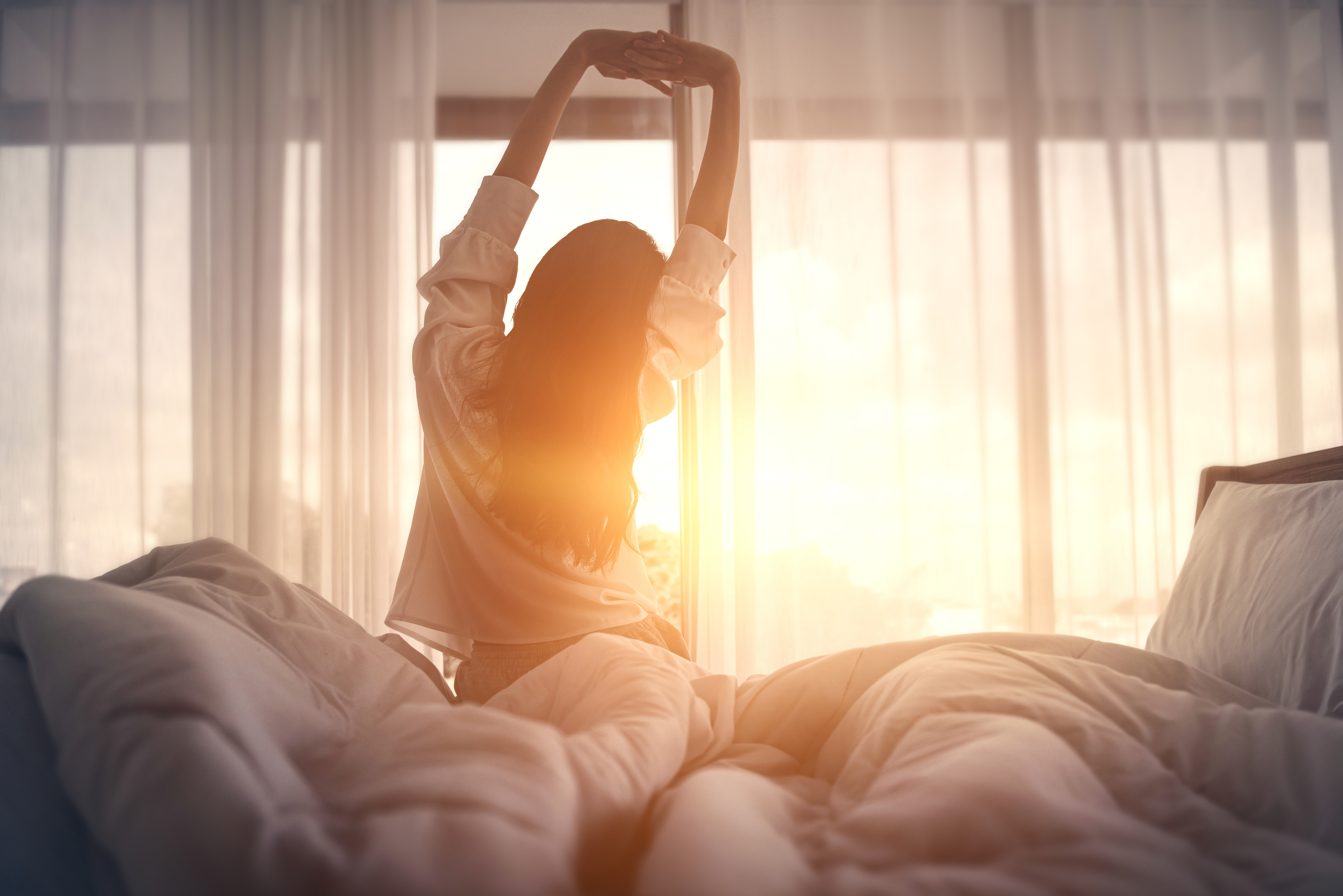 Frau streckt sich morgens im Bett im Sonnenlicht